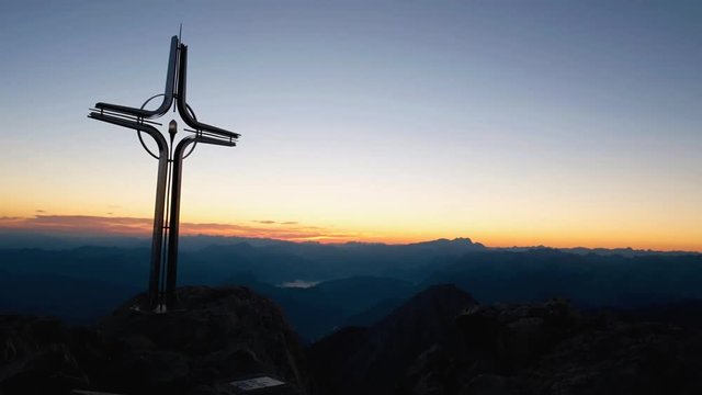 Time lapse of Alps daybreak. Iron cross at mountain top in alp. Cross on top of a mountains peak as typical in the Alps. Monument to the dead climbers