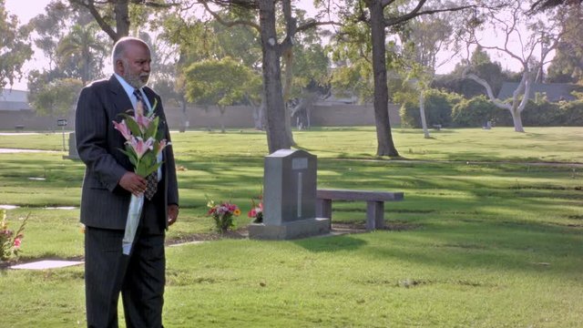 African American mature male holding flowers in a cemetery mourning his loss
