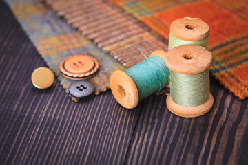 Thimble, buttons, spools of thread and fabric swatches on a wooden background