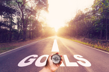 Hand holding compass on Empty asphalt road and Goals concept.