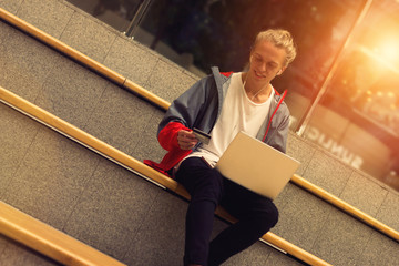 Trendy guy sitting with a laptop and a credit card. Sunlight eff
