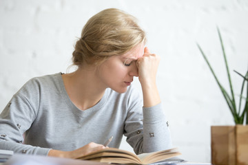 Portrait of a young attractive overworked student girl sitting at the table hands grabbing her...