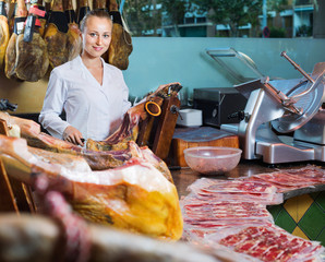 Female seller wearing uniform slicing iberian ham with knife