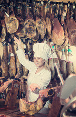 Woman wearing uniform showing  ham in meat shop