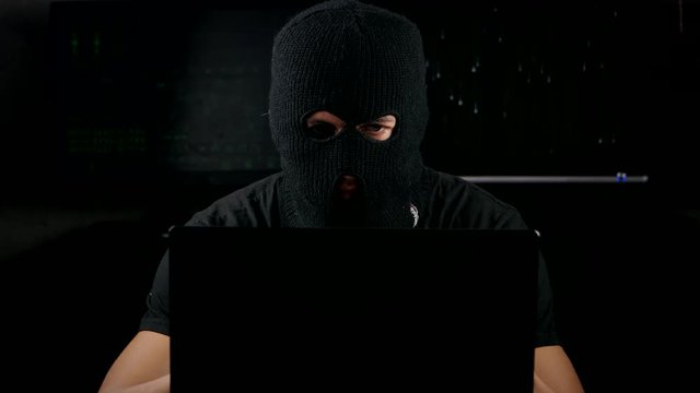 Dangerous hacker in a mask working on a computer in a dark office room