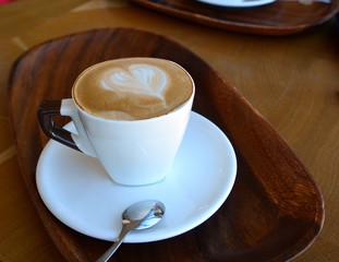 Delicious foamy cappuccino on a white cup on a plate