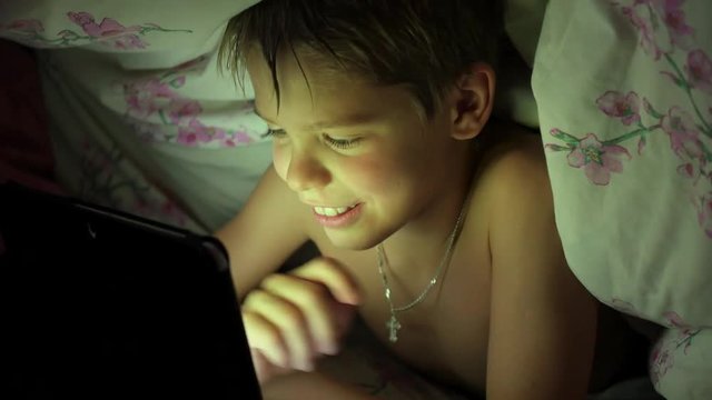 boy lying under blanket and watching cartoons on touch pad