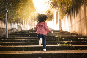 Niña corriendo y saltando por las escaleras mientras se pone el sol al atardecer.