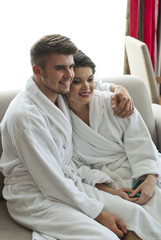 Happy young couple sitting on couch in bathrobe 