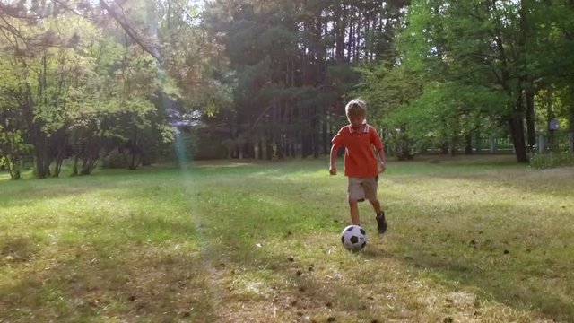 Young boy playing soccer in the park.  Slow motion. Little child kicking football outdoors.