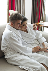 Happy young couple sitting on couch in bathrobe 