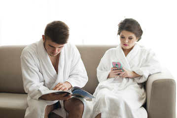 Obraz premium Attractive young couple are looking at smartphone on couch in bathrobe 