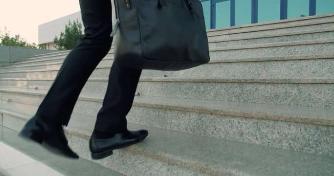 Businessman holding a business briefcase, climbing the stairs in the business centre, slow motion