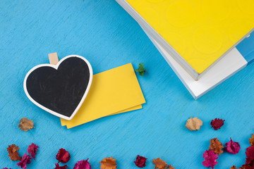 Black heart with note paper,Book and flowers on blue wooden floo