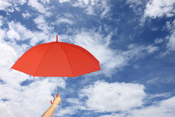 Red umbrella in hand on blue sky and cloud background.
