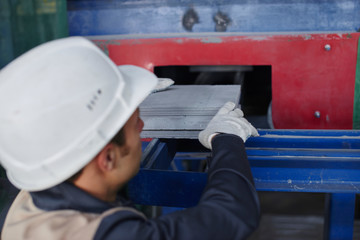 A man in overalls and a helmet stands near a kiln and holding a brick