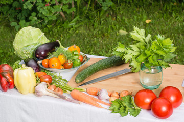 Разделочная доска, нож и овощи на столе на фоне газона