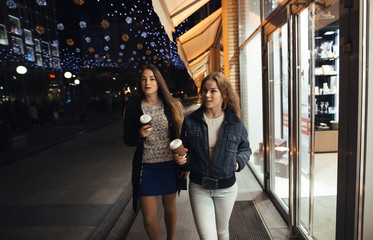 Two stylish girlfriends walking in city avenue at night