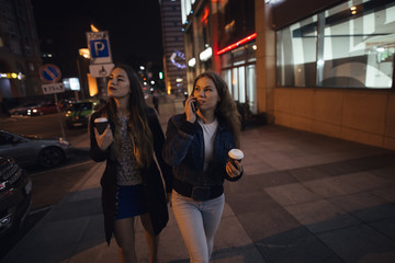 Fototapeta na wymiar Two stylish girlfriends walking in city avenue at night