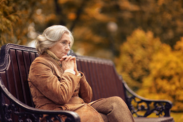 Sad elderly woman sitting on a bench in autumn park
