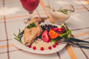 Gourmet roasted rabbit leg with rice and beans. White sauce and glass of tomato juice. Meal is served on white simply plate and checked table cloth, with cutlery. Health and light meal good for diet.