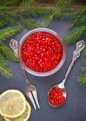 Red salmon caviar in a jar and a spoon with a lemon on the table. Traditional Russian new year delicacy. Selective focus