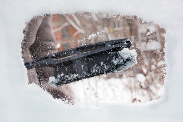 hand cleaning snow-covered window of car with brush