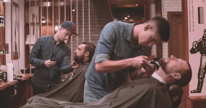Hairdressing process at barbershop 4k video. Barbers working with lumberjack client: cutting man's beards with clipper and scissors