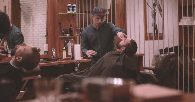 Barbers works in lumberjack barbershop 4k video. View of vintage interior: whisky bottle, glass, retro book