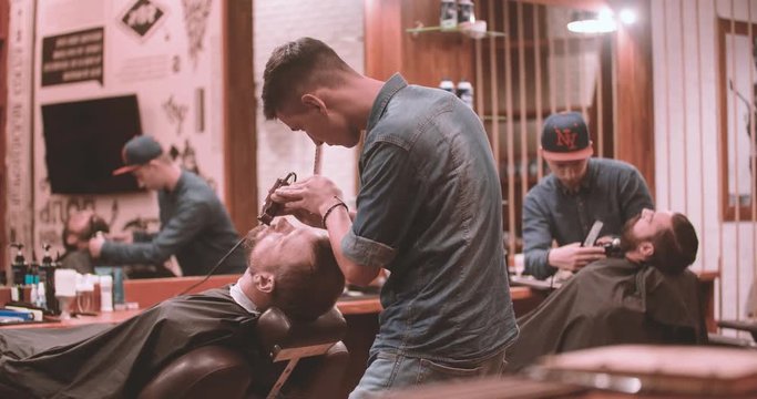 Hairdressing process at vintage barbershop 4k video. Barbers working with lumberjack client: cutting man's beards with clipper