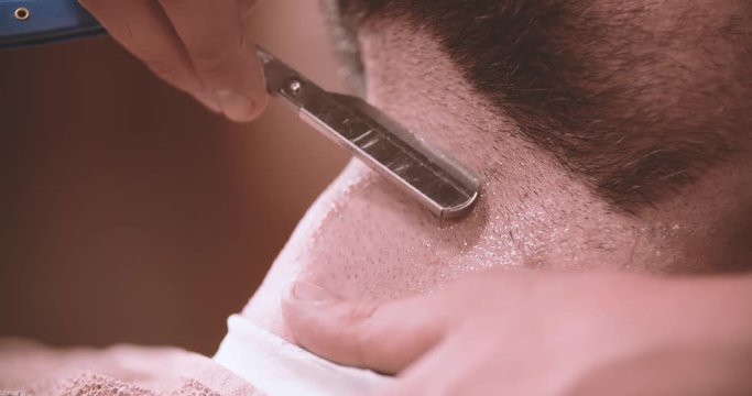 Barber hand shave beard with straight razor 4k video in barbershop. Extremely close-up view of client man neck