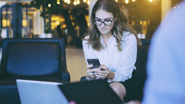Young business woman sitting on a leather chair in the lobby and looks at the screen of the smartphone, is in her hands.Woman surfing the internet on your smartphone while sitting in a chair.