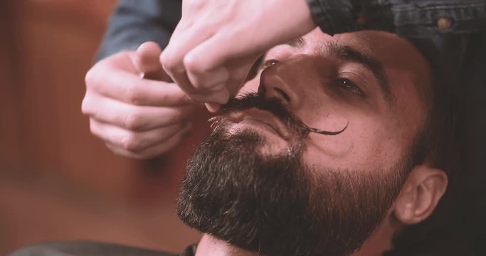 Barber grooming mustache curls and beard with wax in barbershop 4k close-up video. Bearded lumberjack style man