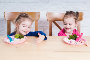 Two little girl eat delicious broccoli for dinner