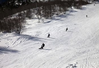 Skiers and snowboarders on ski slope at sun winter day