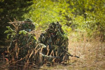 two men in camouflage sitting in the grass