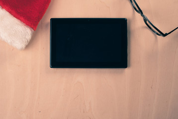 Black tablet in a red Santa Claus hat and glasses,