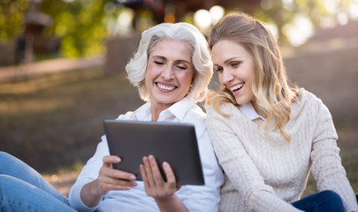 smiling women sitting on the ground and using tablet.