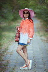 Beautiful young woman in elegant hat and sunglasses posing outdo