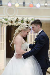 Wedding couple in the restaurant is dancing. Beautiful model girl in white dress. Handsome man in suit. Beauty bride with groom. Female and male portrait. Woman with lace veil. Lady and guy indoors