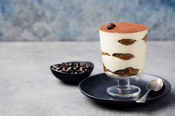 Tiramisu, traditional Italian dessert in glass on a grey stone background Copy space