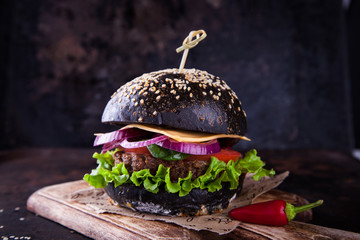 Beef burger with a black bun,with chilli,with lettuce and mayonnaise and ketchup served on pieces of brown paper , on a dark background.selective focus