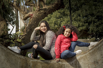Niña y adolescente, hermanas felices en el parque espalda contra espalda.