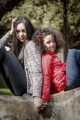 Niña y adolescente, hermanas felices en el parque espalda contra espalda.