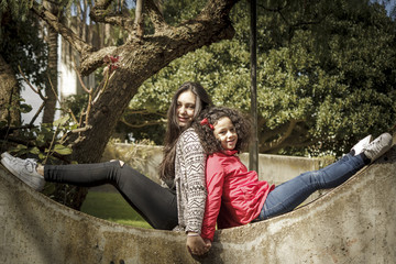 Niña y adolescente, hermanas felices en el parque espalda contra espalda.