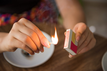 Closeup of female hands lighting a match on box with flame and plates