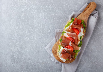 Sandwich with ciabatta, prosciutto,brie cheese and lettuce.on the Board, a grey stone background.