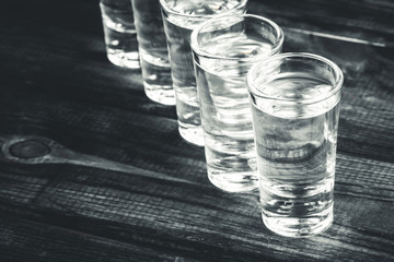 Vodka shots filled with alcohol on wooden black bar.