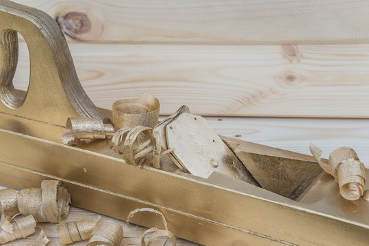 Golden jack-plane with golden shavings on a wooden background