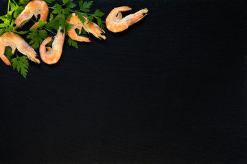 Preparing fresh seafood in the kitchen with gourmet pink shrimp surrounded by fresh parsley on black stone background